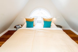 Ein Schlafzimmer mit einem Bett, Kissen, einem kleinen Tisch und einem Fenster.
