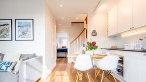 A modern kitchen with white cabinets, a dining area with white chairs, and a staircase leading to an upper level. - Höög Hüs, Whg. 4 - Höög Hüs (Sylt)