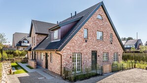 A two-story brick house with a sloped roof, a front porch, and a gravel driveway. - Höög Hüs, Whg. 4 - Höög Hüs (Sylt)