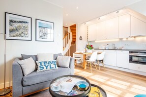 Ein modernes Wohnzimmer mit einem grauen Sofa, einem Couchtisch mit Tablett und einem Essbereich mit Holztisch und Stühlen.