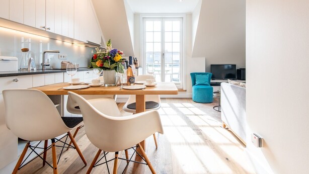 A modern kitchen with white cabinets, a wooden dining table, and two white chairs. - Höög Hüs, Whg. 4 - Höög Hüs (Sylt)