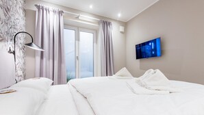 Hotellihuone, jossa on kaksi sänkyä, taulutelevisio, ikkuna verhoilla ja lamppu.