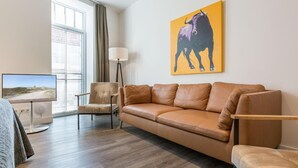 Un salon moderne avec un canapé en cuir, un téléviseur à écran plat, un lampadaire et un grand tableau représentant un taureau accroché au mur.