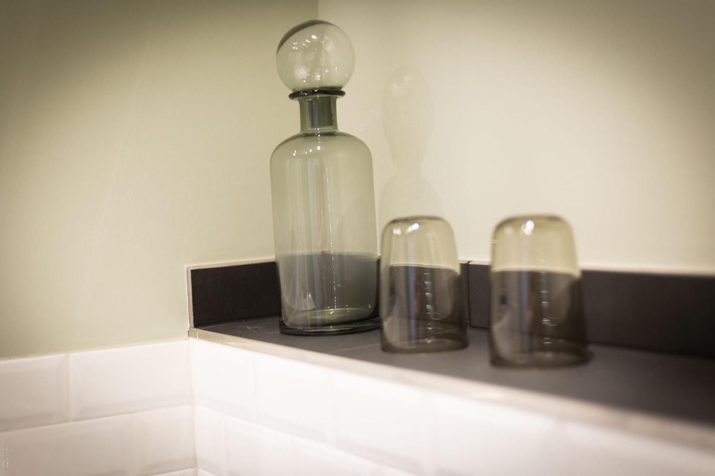A bathroom shelf with a glass bottle and two salt and pepper shakers.