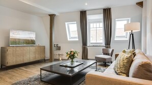 A modern living room with a flat-screen TV, a wooden cabinet, a coffee table with a vase of flowers, a sofa, and a floor lamp. - Art your Life - Residence, Whg. 9 Iliya - Art your Life - Residence Seeburg (Sylt)
