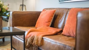 A brown leather sofa with orange cushions and a throw blanket.