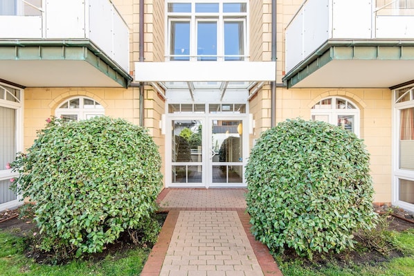A building with a central entrance, two symmetrical bushes, and a brick pathway leading to the entrance.