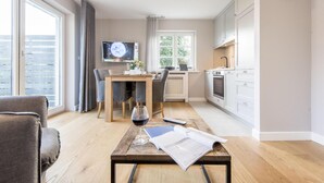 A modern living room with a wooden coffee table, a sofa, and a dining area with a table and chairs. - Ringhoog-Hüs, Whg. 2 "Waldidyll" - Ringhoog Hüs (Sylt)