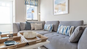 A modern living room with a grey sofa, patterned cushions, a wooden tray with a bowl, and a framed picture on the wall. - House Nordmarkgarten, Whg. 5 - House Nordmarkgarten (Sylt)