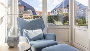A modern living room with a blue armchair, a small table, and a view of neighboring houses through large windows. - House Nordmarkgarten, Whg. 5 - House Nordmarkgarten (Sylt)