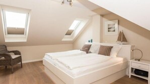 A bedroom with a large bed, a chair, a nightstand, and a window.