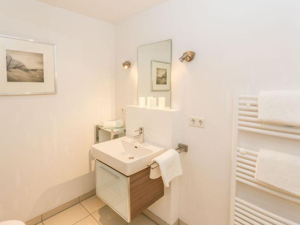 Un baño moderno con un lavamanos blanco, espejo y toallero.