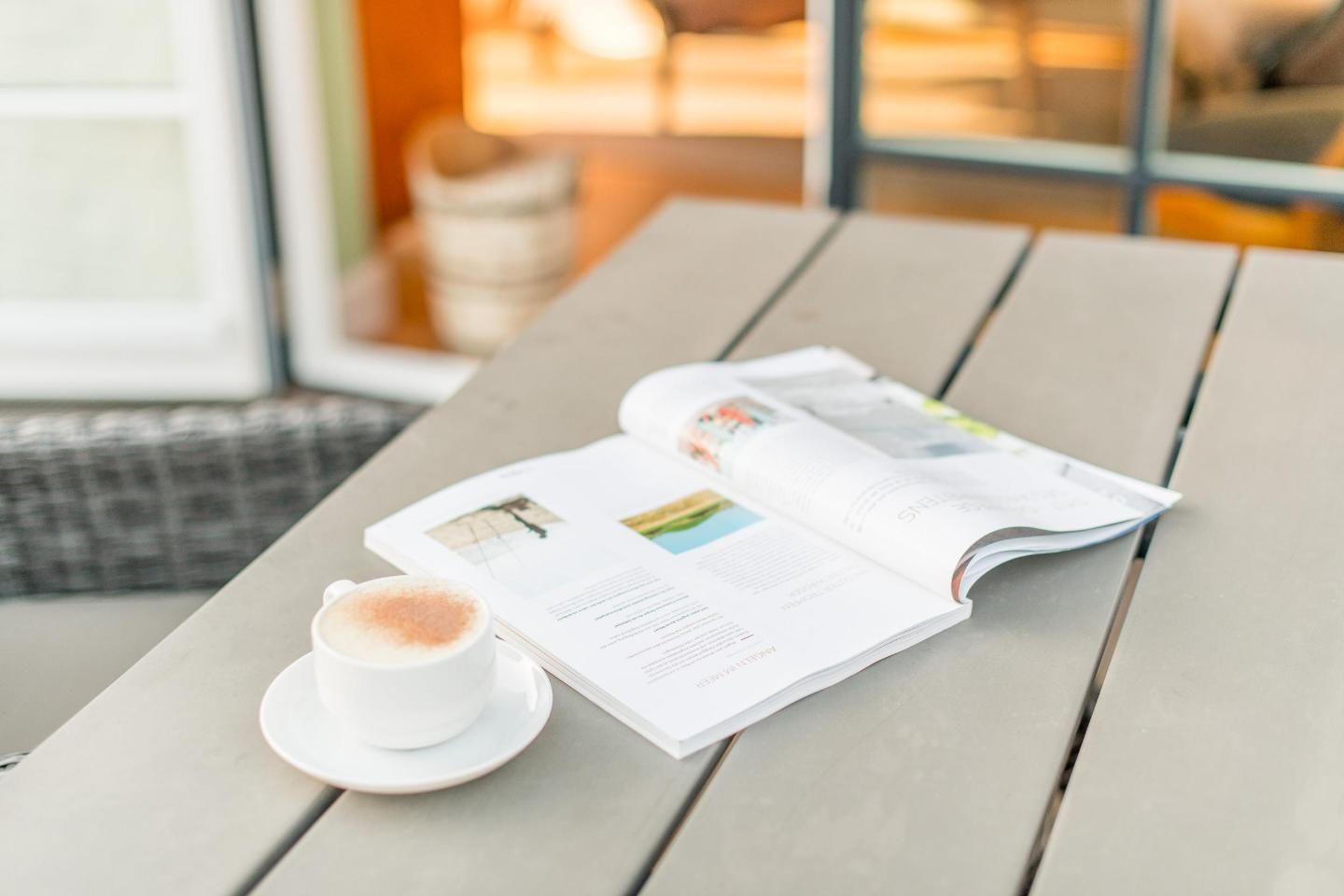 A magazine open on a wooden table with a cup of coffee beside it.