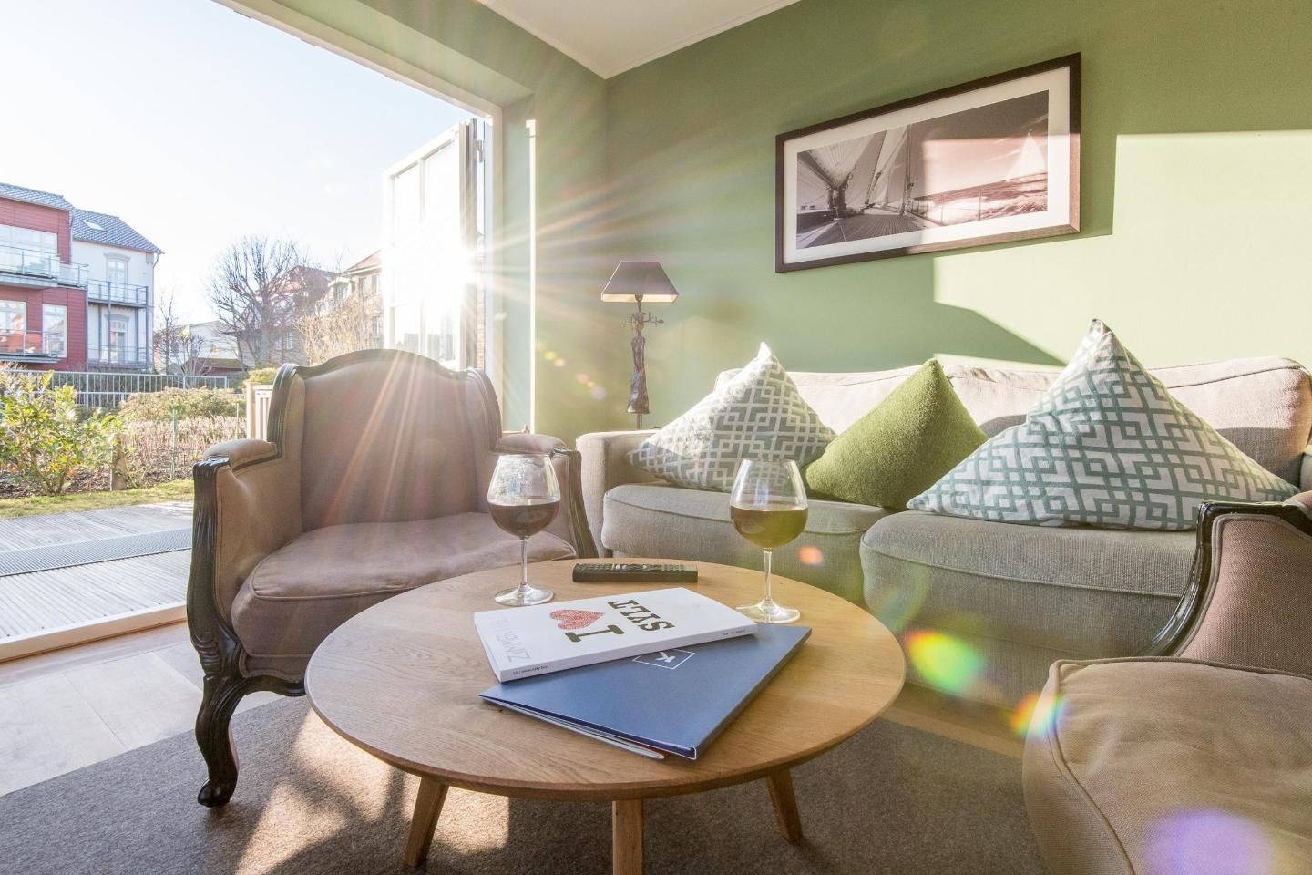 A cozy living room with a sofa, armchair, and coffee table. There are two glasses of wine and a book on the table.