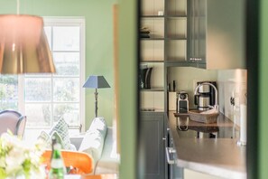 A modern kitchen with a coffee machine, a kettle, and a sink. There is a window with a view of greenery outside. - Villa Maybach, Whg. 4 Grüner Wim - Villa Maybach (Sylt)
