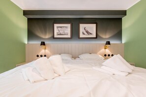 A neatly made bed with white linens and two pillows, flanked by two bedside tables with lamps. - Villa Maybach, Whg. 4 Grüner Wim - Villa Maybach (Sylt)