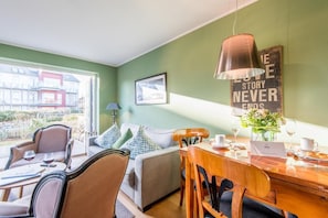 Un'accogliente zona pranzo con un tavolo in legno, sedie e un portatile. Si nota una parete verde con un quadro incorniciato e un cartello con su scritto "STORY NEVER ENDS".