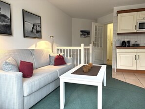 Una sala de estar con sofá, una mesa de centro y una zona de cocina con armarios y microondas.