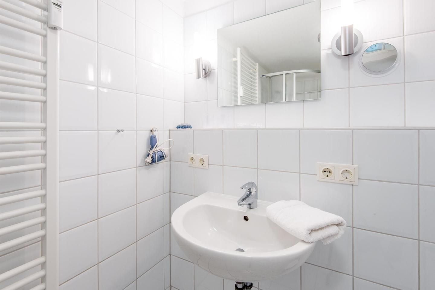 A modern bathroom with white tiles, a white sink, a mirror, and a towel hanging on the wall.