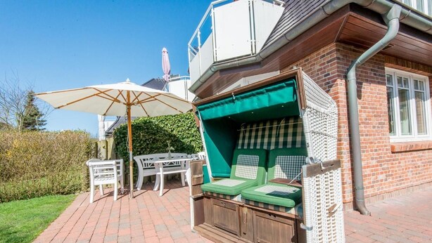 Eine Terrasse mit Tisch und Stühlen, eine überdachte Sitzecke mit Kissen und einem weißen Sonnenschirm.