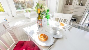 Ein Frühstückstisch gedeckt mit Tellern, Tassen und einer Wasserflasche, mit einem roten Kissen und Blick aus dem Fenster.