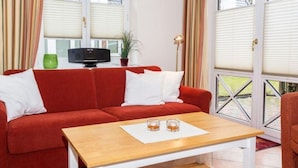 En rød sofa med hvide puder, et træsofabord og en lille, hvid måtte.