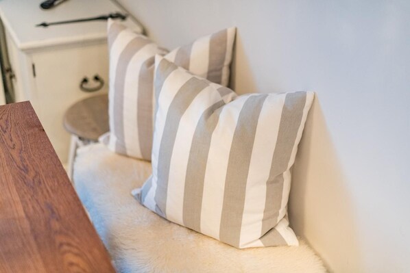 Una cama con almohadas a rayas, una mesita de madera y una manta suave y blanca.