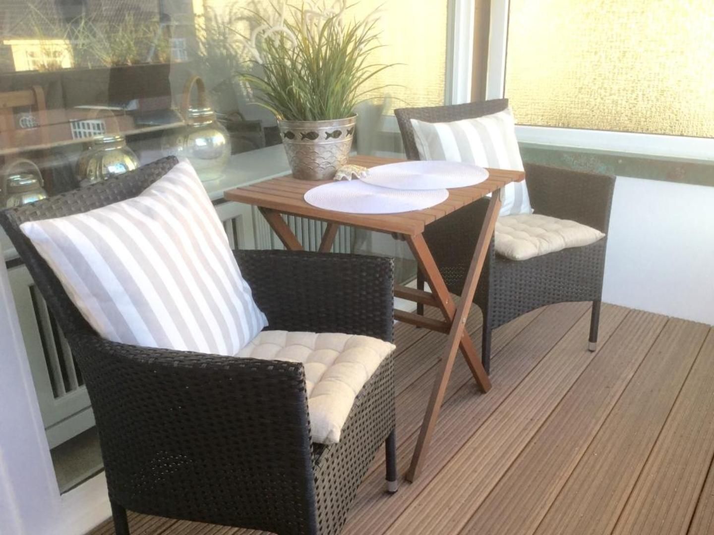 Ein Balkon mit Korbstühlen, einem Tisch mit weißen Tellern und einem Blumentopf.