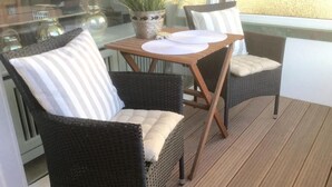 Ein Balkon mit Korbstühlen, einem Tisch mit weißen Tellern und einem Blumentopf.