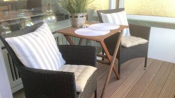 Ein Balkon mit Korbstühlen, einem Tisch mit weißen Tellern und einem Blumentopf.