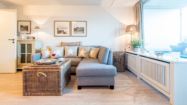 Ein modernes Wohnzimmer mit grauem Sofa, Korbohase und einem großen Fenster mit Aussicht.