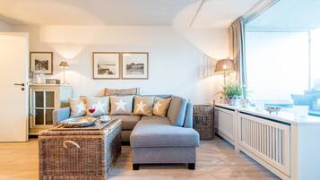 Ein modernes Wohnzimmer mit grauem Sofa, Korbohase und einem großen Fenster mit Aussicht.