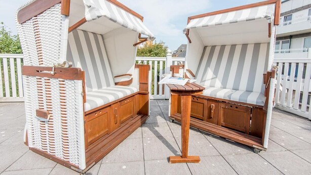 Two wooden lounge chairs with striped cushions and a small wooden table, set on a tiled patio with a white fence in the background. - Bädervilla, Whg. 28a - Bädervilla (Sylt)