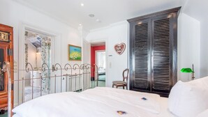 A bedroom with a large bed, a wardrobe, a chair, and a painting on the wall. - Bädervilla, Whg. 28a - Bädervilla (Sylt)