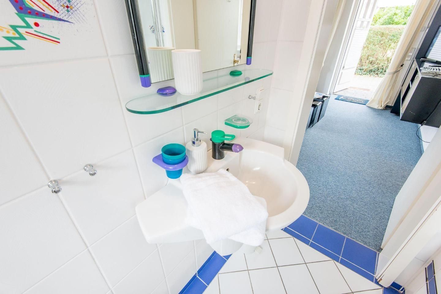 A bathroom with a white sink, a mirror, and a glass shelf with toiletries.