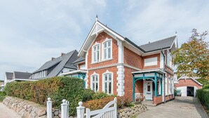 A two-story house with a brick facade, white trim, and a front porch with a blue awning. - Bädervilla, Whg. 28b - Bädervilla (Sylt)