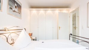 A hotel room with a large bed, a bedside table with a lamp, a wardrobe, and a mirror on the wall. - Bädervilla, Whg. 28b - Bädervilla (Sylt)