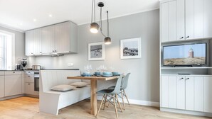 A modern kitchen with a dining area, white cabinetry, and a television on the wall.