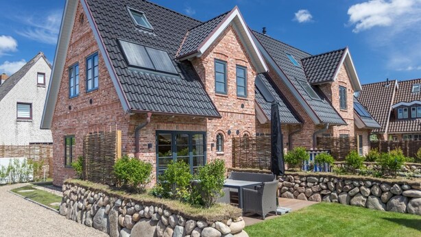A brick house with a sloped roof, stone walls, and a well-maintained garden.