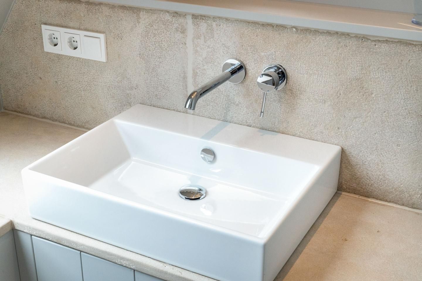 A white rectangular sink with a chrome faucet, a single round drain, and a beige textured wall.