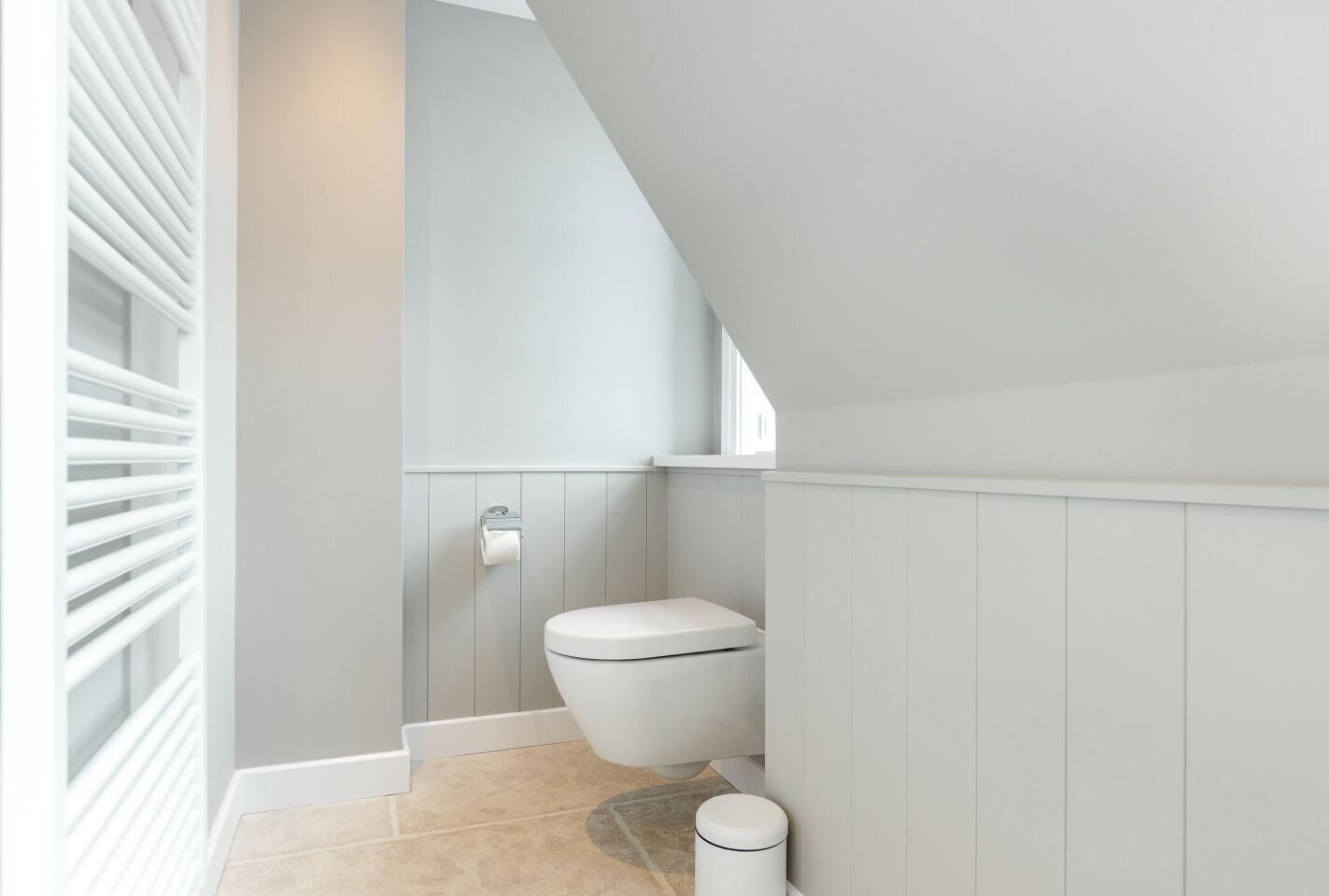 A modern bathroom with a white toilet, a towel rack, and a small trash bin.