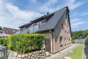 Een bakstenen huis met een schuin dak, een stenen muur en een verzorgde haag.
