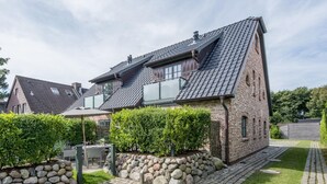 Una casa de dos pisos con techo inclinado, base de piedra y entrada pavimentada.