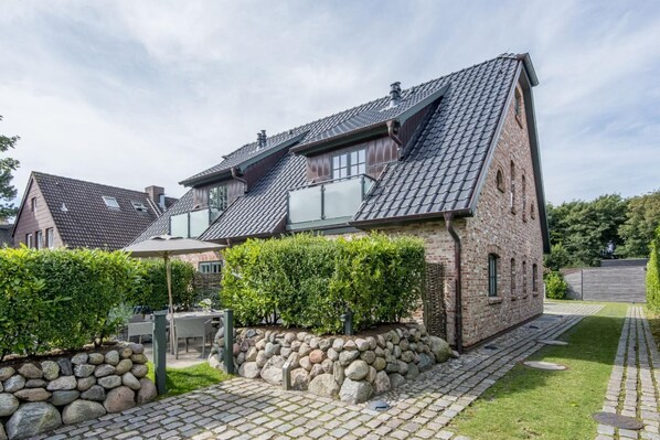 Een twee verdiepingen tellend huis met een schuine kap, stenen fundering en een geplaveid oprit.