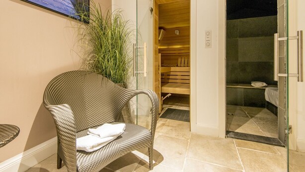 Una habitación con una silla de mimbre, cabina de ducha de vidrio y un banco de madera.