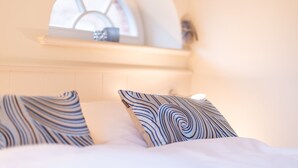 Una cama con almohadones estampados, una ventana con vistas y un estante con un objeto decorativo.