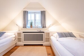 Een slaapkamer met twee bedden, een raam met gordijnen, een radiator en een kleine plant op de vensterbank.