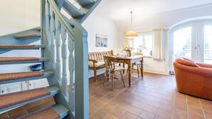 Eine Treppe mit blauen Stufen und einer Holzbank, ein Essbereich mit Tisch und Stühlen sowie ein Sofa in einem hellen Raum mit Aussicht.