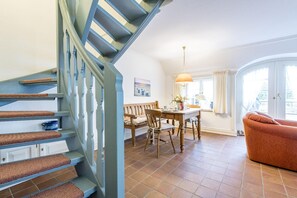 Una escalera con escalones azules y un banco de madera, un comedor con una mesa y sillas, y un sofá en una habitación luminosa con vistas.