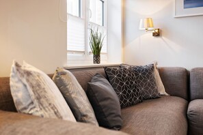 A living room with a sofa, decorative pillows, a potted plant, and a wall-mounted lamp. - House at Steinmannstraße 77, half of House A (Sylt)